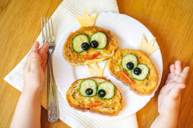 Yaratıcı çocukların kahvaltısı, çocukların elleri bir tabak kızarmış ekmeği kurbağa menüsü şeklinde tutuyor..