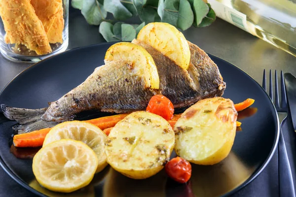 Frischer gebratener Fisch Dorada mit verschiedenen Gemüsesorten auf dem schwarzen Dis — Stockfoto