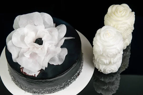 Big homemade black cake decorated with white flower and white ca