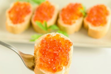 Beyaz ekmeğin üzerinde kırmızı havyar ve çatal var.