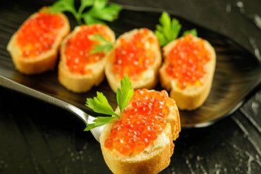 Siyah çatalın üzerinde beyaz ekmek ve kırmızı havyar.