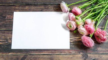 Ahşap arka planda pembe yumuşak ranunculus buketi yakın plan. Mesajlaşmak ve selamlamak için beyaz çerçeveli. Tatil karşılama konsepti, klasik tasarım. 