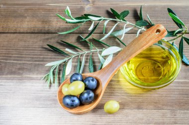 Ahşap arka planda yeşil ve siyah zeytin kaşık, zeytin yağı kasesi ve zeytin ağacı dalları. Güzel ışık, sağlıklı yemek.. 