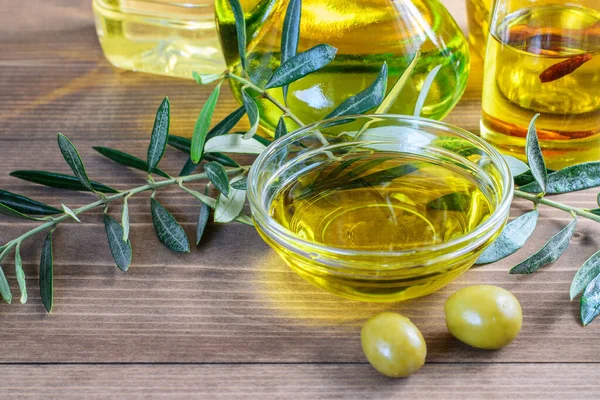 Olive oil bottles, glass bowl with olive oil and olive tree branches on the wooden table in sunlights. Healthy food concept.