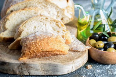 Ahşap mutfak kesme tahtasının üzerinde beyaz ev yapımı ekmek dilimleri, zeytin yağı şişesi ve koyu arkaplanda olyalar.. 