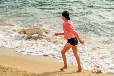 Deniz sahilinde köpeğiyle oynayan bir kız. Açık hava aktiviteleri, sağlıklı yaşam tarzı.. 