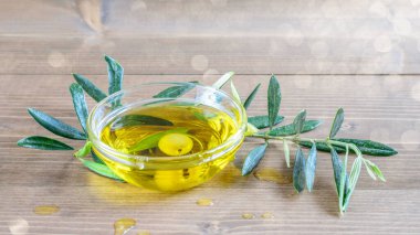 Cam bir kasede zeytin yağı, ahşap masada zeytin dalı. Güneş ışığı, güzel güneşli bokeh. 