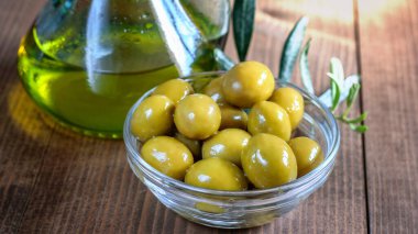 Cam bir kasede yeşil zeytin ve güneş ışığında ahşap masada zeytin yağı şişesi. Sağlıklı beslenme konsepti. 