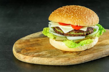 Hamburger vejetaryeni. Tahta kesme tahtasının üzerinde ıspanak pirzolası, soğan, salatalık, domates ve peynirli burger. Vejetaryenler için ıspanak pirzolası ile lezzetli bir burger.. 