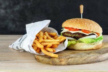 Hamburger vejetaryeni, ıspanaklı pirzola, sebze ve peynir ahşap mutfak kesim tahtasında. Ekolojik kağıt torbada kızarmış patates. Hafif fast food konsepti. 