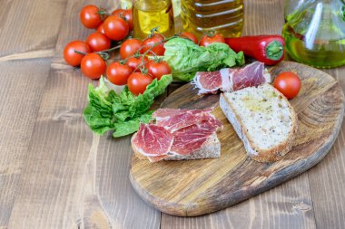 Mutfak kesim tahtasının üzerinde dilimlenmiş jambon ve ekmek. Domates kirazı, dolmalık biber, yeşil marul ve mutfak masasında zeytinyağı karışımı. Sağlıklı gıda konsepti. 