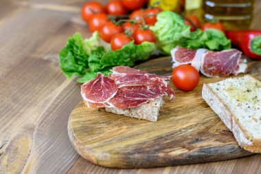 Taze jamonlu sandviç, kirazlı domates, ahşap mutfak masasında yeşiller. Atıştırmalık sağlıklı yemek.. 