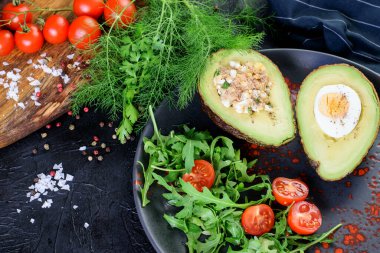Ton balığı, sos ve yumurtalarla doldurulmuş ketojenik diyet avokadosu. Arugula, domatesler vişne ve dereotu siyah arka planda. Yemek için sağlıklı keto diyet avokado.. 