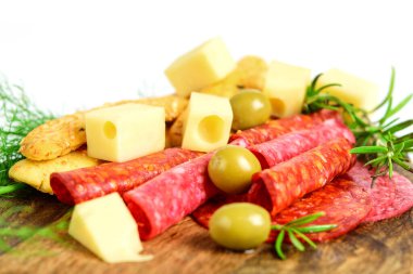 Dilimlenmiş peynir, salam, sucuk, yeşil otlar, zeytin ve ekmek çubukları tahta kesim tahtasında, beyaz arka plan. Atıştırmalık sağlıklı yemek.. 