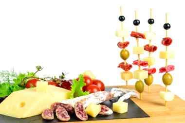 Zeytin kanapeleri, peynir dilimleri, sucuk, salam ve elma. Tapas tahtasında taze et, emmental peynir, domates, kiraz ve yeşil otlar var. Beyaz arkaplan, alanı kopyala. 