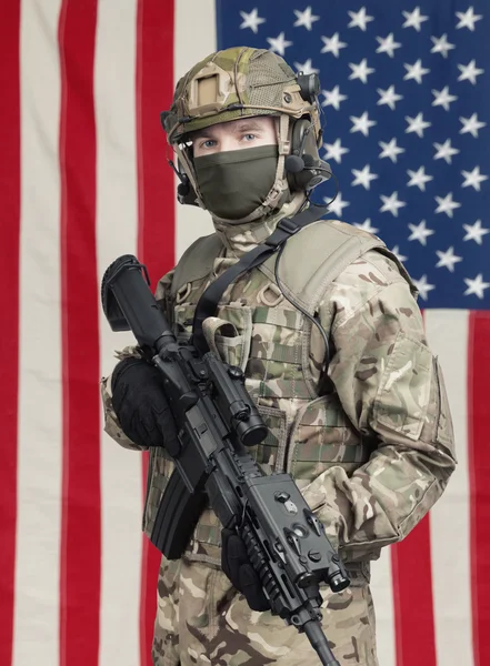 Amerikai katona géppisztollyal a kezében, és az amerikai zászló a háttérben — Stock Fotó