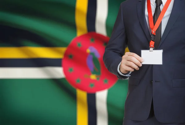 Affärsman som innehar kortet namnskylt på en snodd med en flagga på bakgrunden - Dominica — Stockfoto