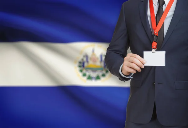 व्यवसायी पृष्ठभूमि पर राष्ट्रीय ध्वज के साथ एक लंगर पर नाम कार्ड बैज पकड़ रहा है अल साल्वाडोर — स्टॉक फ़ोटो, इमेज