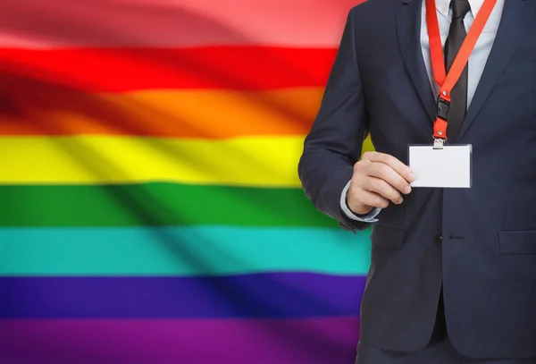 Empresario sosteniendo credencial tarjeta sobre un elemento de amarre con bandera sobre fondo - Lgbt — Foto de Stock