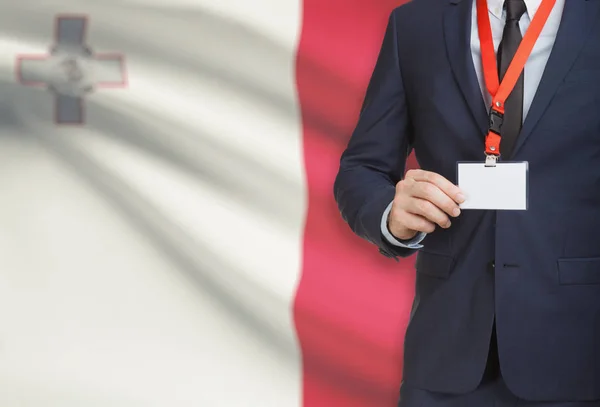 Uomo d'affari holding badge in carta su un cordino con una bandiera nazionale su priorità bassa - Malta — Foto Stock