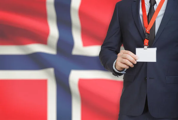 Uomo d'affari holding badge in carta su un cordino con una bandiera nazionale su priorità bassa - Norvegia — Foto Stock