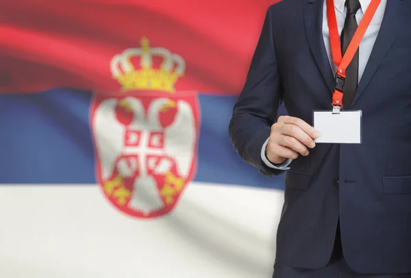 Uomo d'affari holding badge in carta su un cordino con una bandiera nazionale su priorità bassa - Serbia — Foto Stock