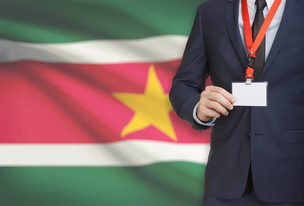 Biznesmen gospodarstwa karta identyfikator na smyczy z flagi narodowej na tle - Surinam — Zdjęcie stockowe