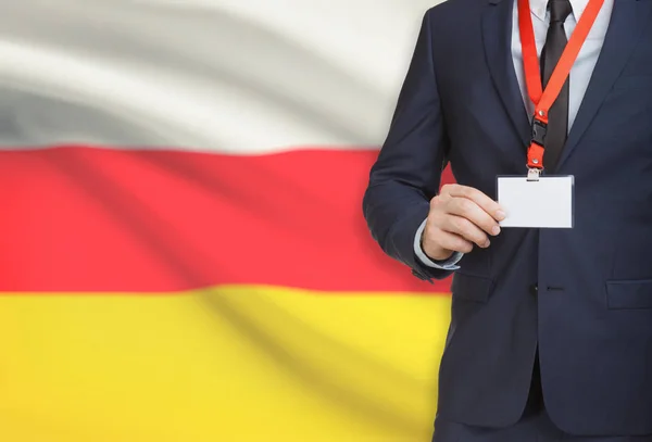 Affärsman som innehar kortet namnskylt på en snodd med en flagga på bakgrunden - Sydossetien — Stockfoto