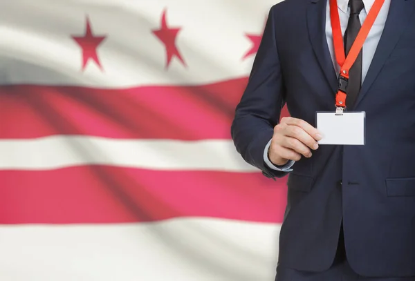 Empresario celebración tarjeta de identificación en un elemento de amarre con bandera de estado de Estados Unidos en el fondo - Columbia — Foto de Stock