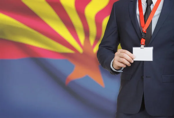 Affärsman innehav märke på en snodd med Usa statsflagga på bakgrunden - Arizona — Stockfoto