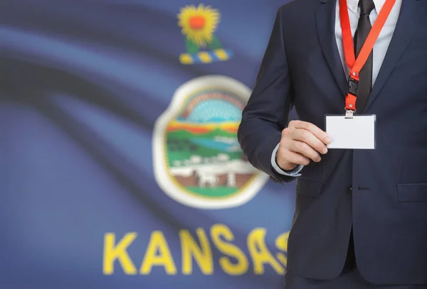 Businessman holding badge on a lanyard with USA state flag on background - Kansas