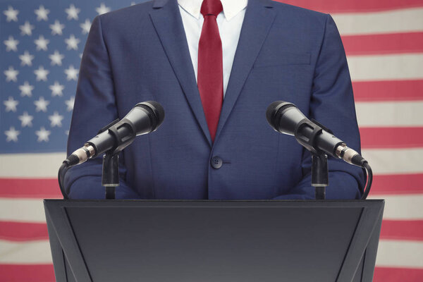 Businessman or politician making speech behind the pulpit with USA flag on background