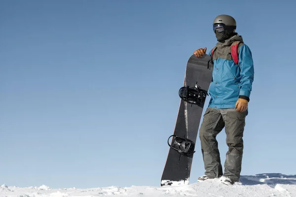 Homme tenant de snowboard et de jeter un oeil au paysage en haut de la montagne avec un ciel bleu sur fond. Image filtrée : Croix traitées effet vintage. — Photo