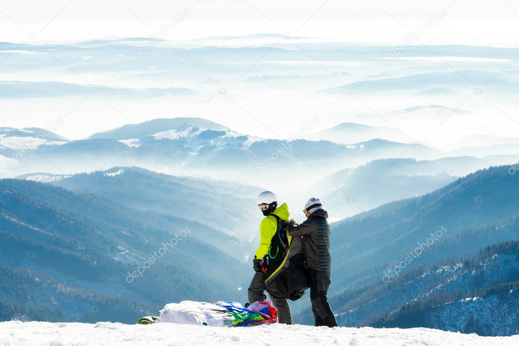 Paragliders getting ready to launch from snowy slope of a mountain