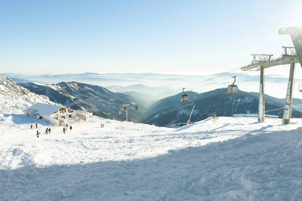 Cabines do teleférico subindo e descendo alto nas montanhas, em uma área de resort de esportes de inverno em um dia ensolarado — Fotografia de Stock