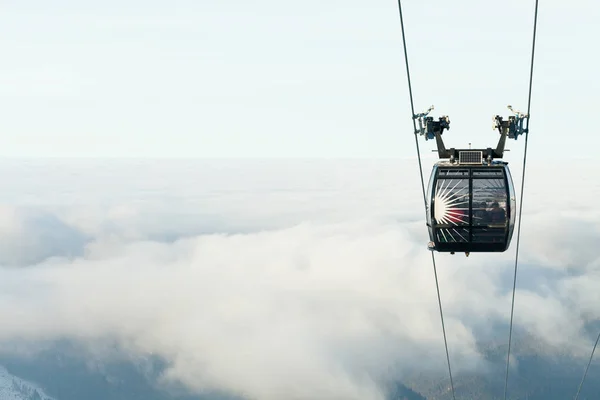 Cabina de teleférico subiendo por encima de las nubes a la cima de una montaña en un resort de esquí — Foto de Stock