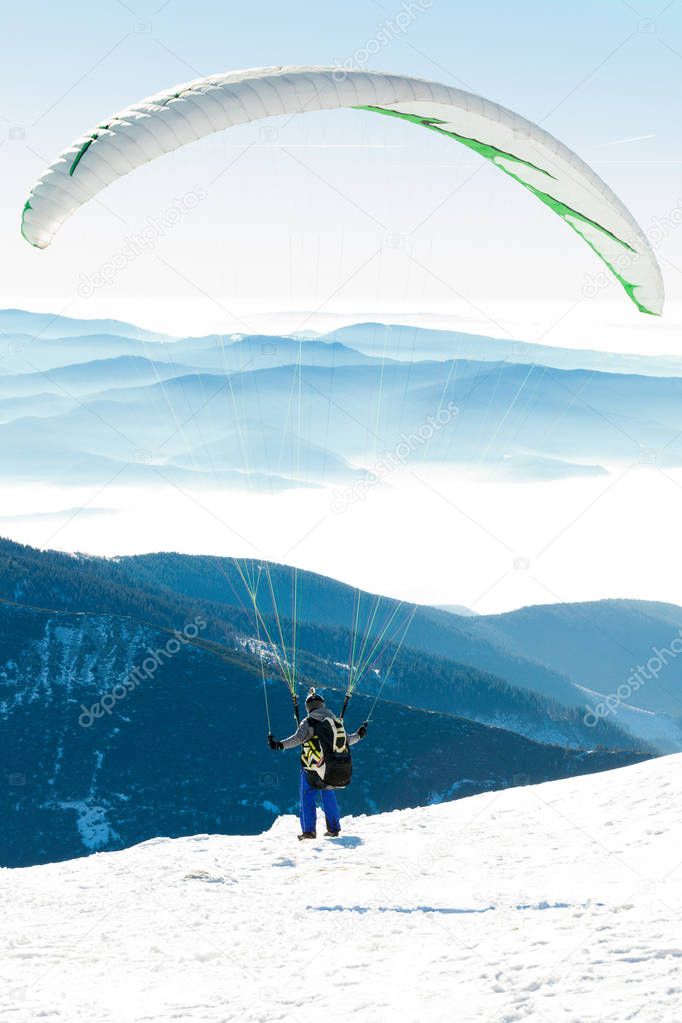Paraglider preparing to get launched from snowy slope of a mountain
