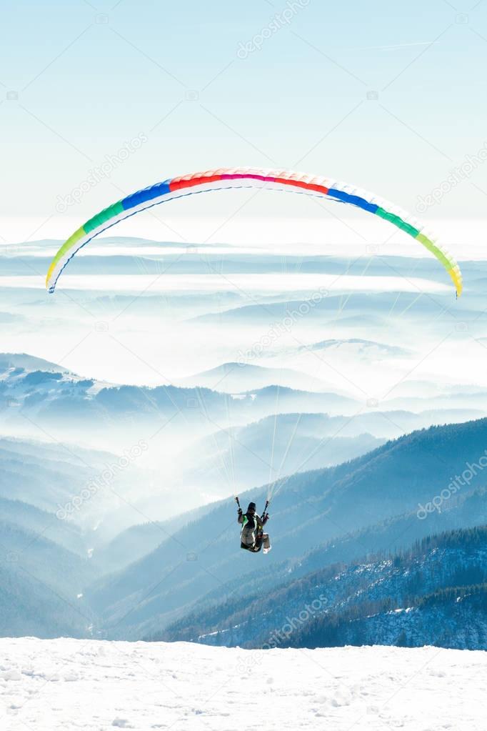 Paragliders launched into air from a snowy slope of a mountain
