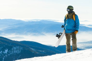 Bir dağın tepesinden bir manzaraya bakarak genç snowboarder