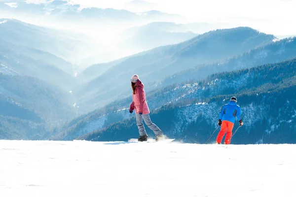 Kvinna snowboardåkare och manliga skidåkare att göra utförsåkning ride från toppen av ett berg — Stockfoto
