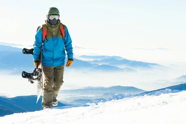 Jonge snowboarder lopen de berg op met snowboard in hand — Stockfoto