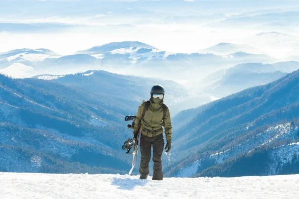 Jonge snowboarder beklimmen van de berg met zijn bord in de hand — Stockfoto