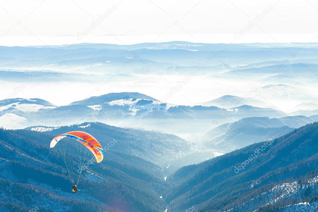 Paragliders launched into air from the very top of a snowy slope of a mountain