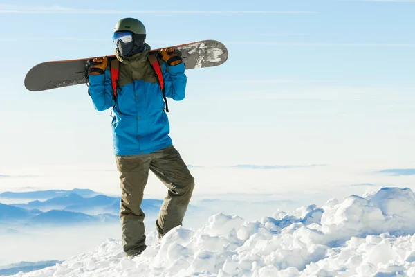 Snowboarder jóvenes en situación de casco en la parte superior de una montaña con el hermoso cielo de fondo —  Fotos de Stock