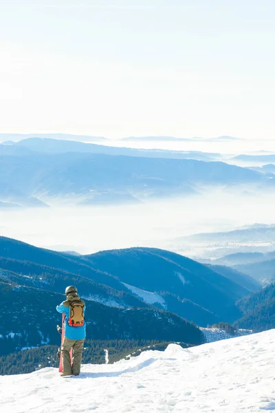 Jonge snowboarder in helm nemend een blik bij landschap van de top van een berg — Stockfoto
