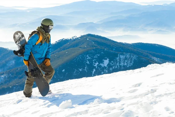 Joven snowboarder de casco a pie en la cima de una montaña —  Fotos de Stock