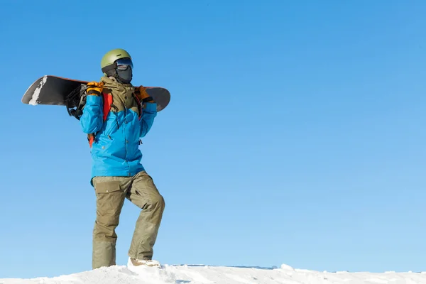 バック グラウンドで美しい空と山の頂上で散歩しているヘルメットの若いスノーボーダー ストック画像