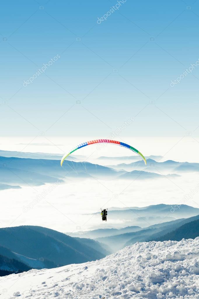 Paraglider in the sky above a snowy slope of a mountain