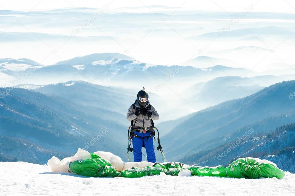 Paraglider in helmet preparing to get launched from snowy slope of a mountain