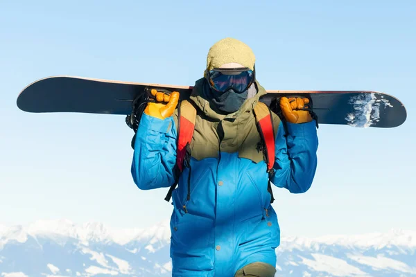 Joven snowboarder en casco con snowboard detrás de su espalda —  Fotos de Stock